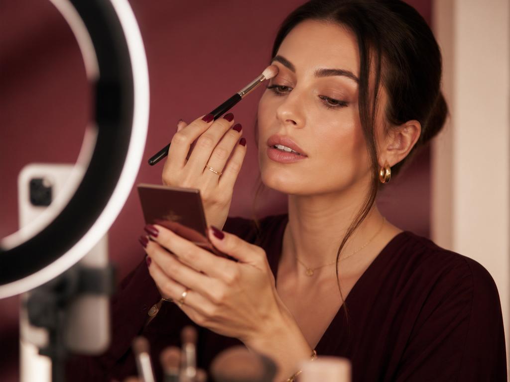 Beauty creator Jade filming a makeup tutorial in a burgundy-toned studio with a ring light